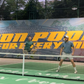 Two people playing on a covered pickleball court with a large banner in the background.