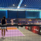 Indoor sports facility with people playing pickleball, blue roof, and promotional banners.