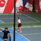 Two people playing pickleball on an indoor court with a large advertisement in the background.