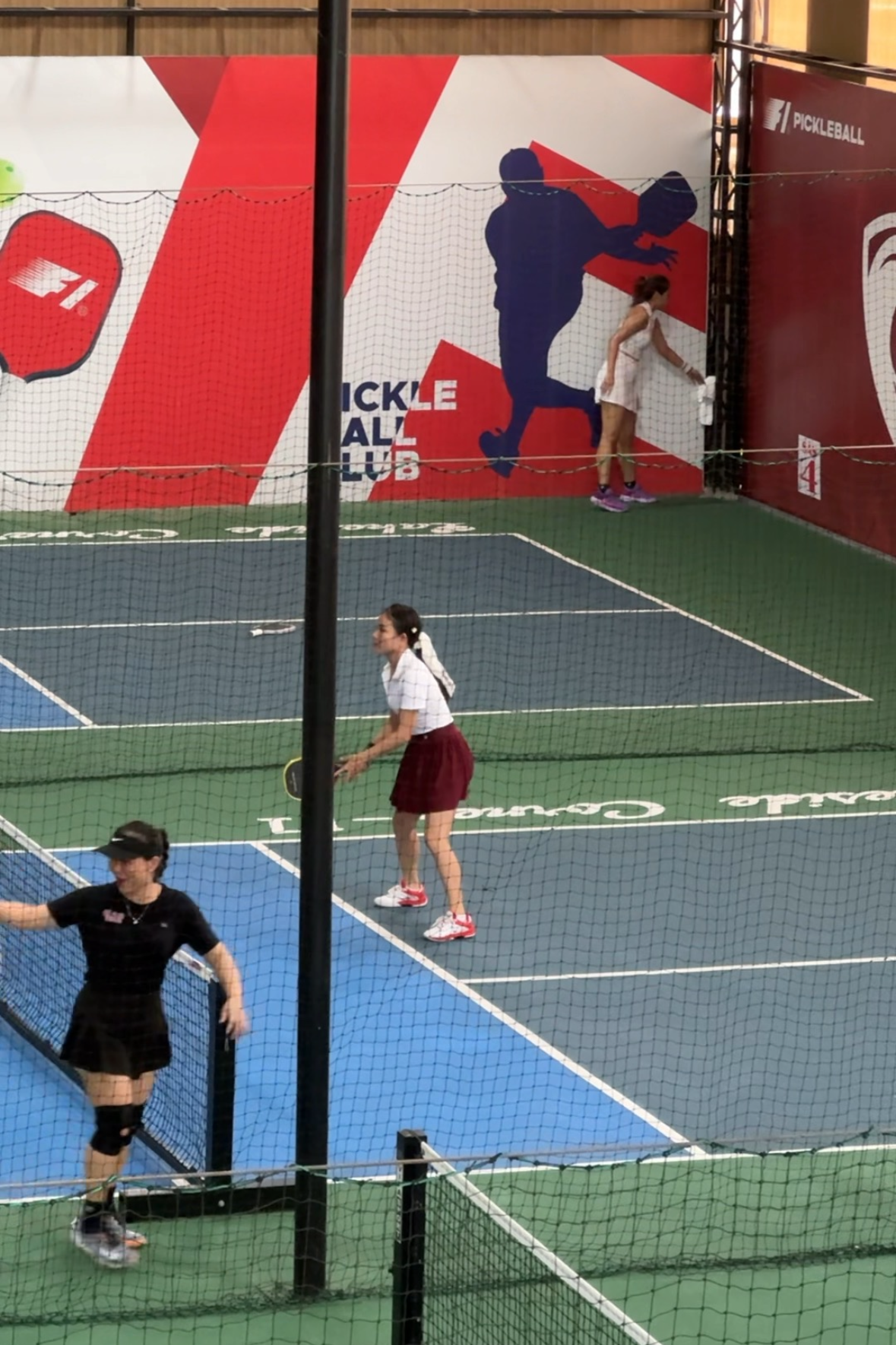 Two people playing pickleball on an indoor court with a large advertisement in the background.