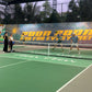 People playing tennis on an indoor court with a banner in the background.