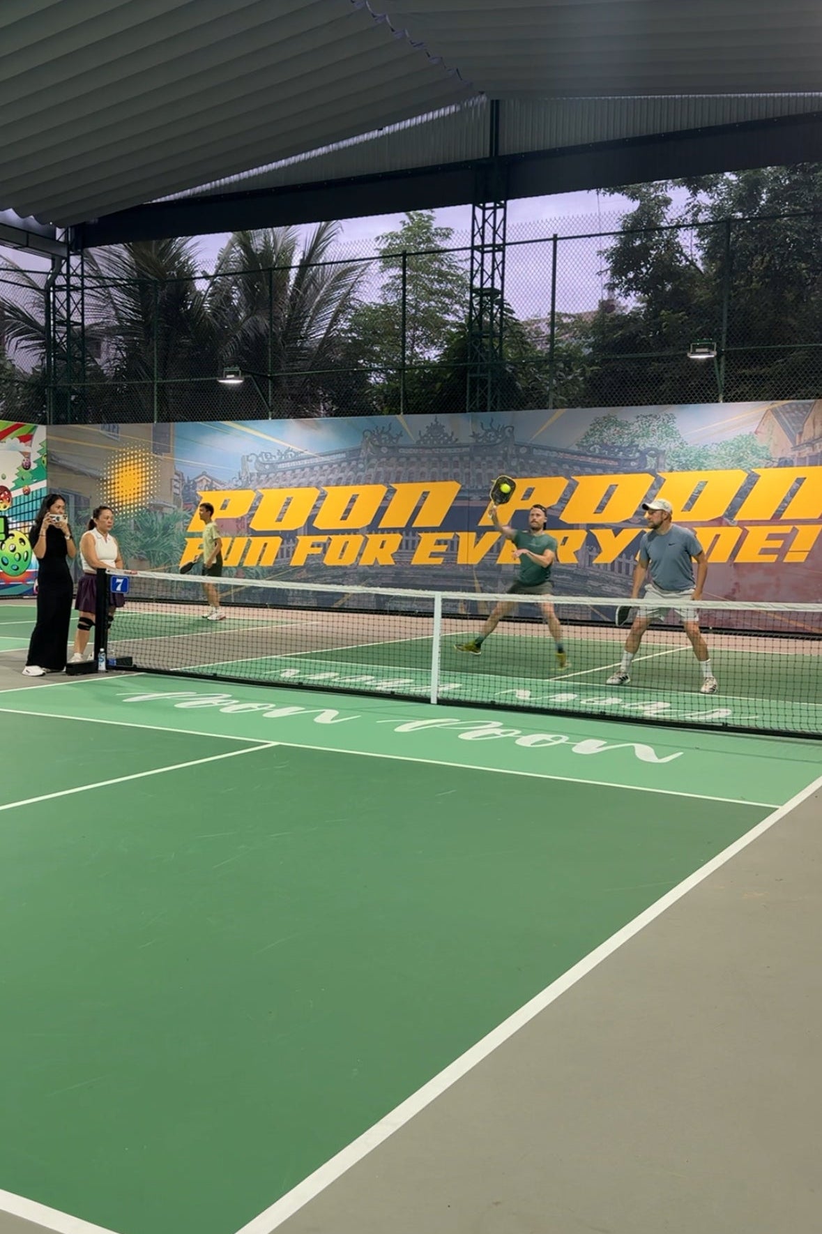 People playing tennis on an indoor court with a banner in the background.