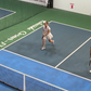 Person playing pickleball on an indoor court with advertisements on the walls.