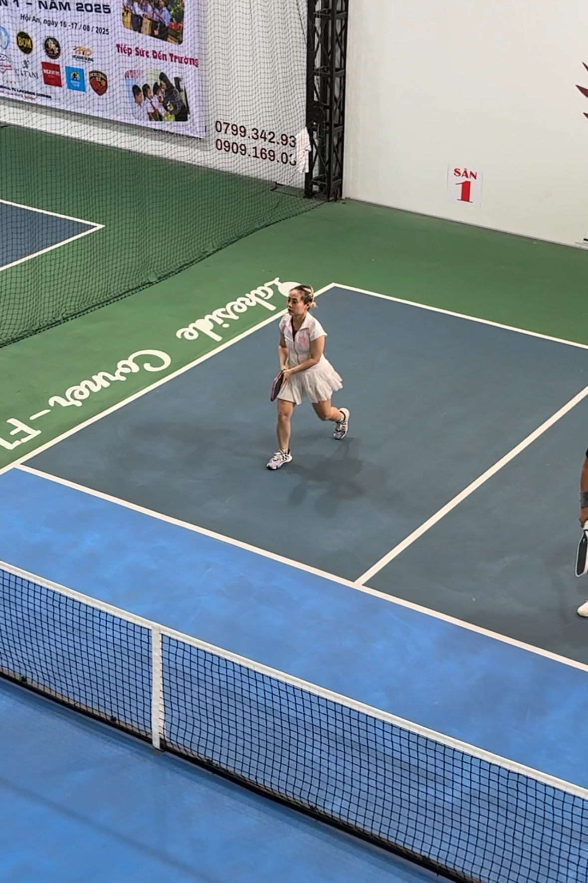 Person playing pickleball on an indoor court with advertisements on the walls.