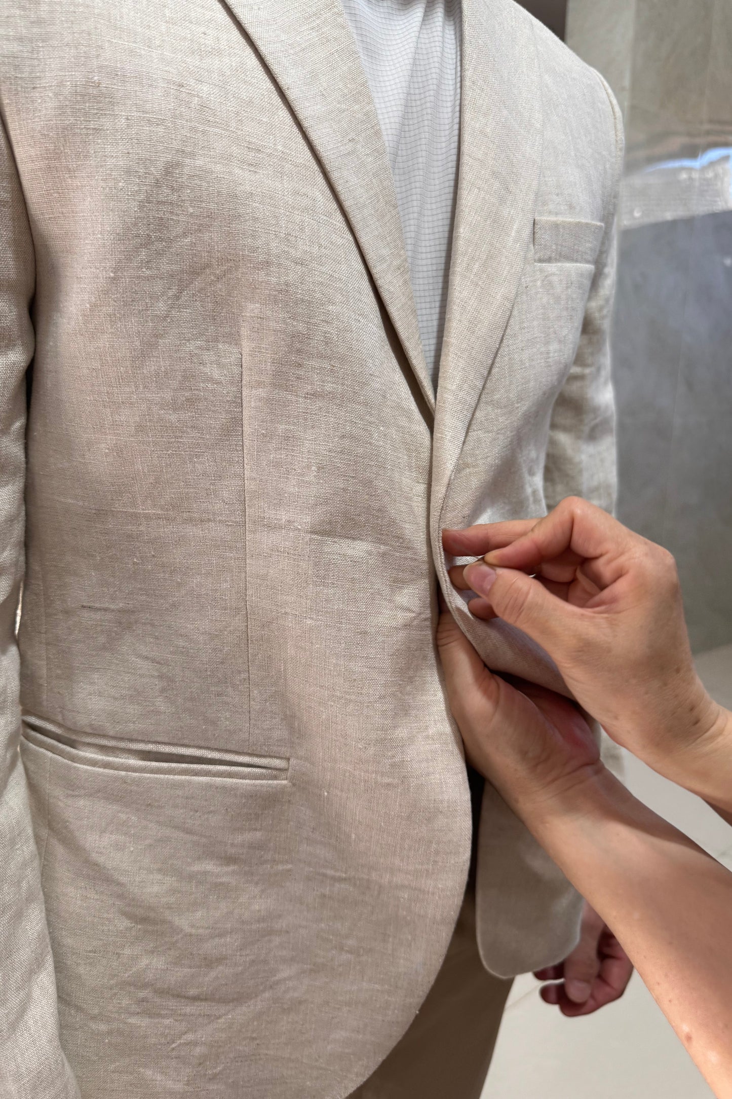 Person adjusting a beige linen garment with a neutral background