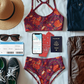 Collection of travel items including a sports bra, shorts, sunglasses, passport, and suitcase on a white surface.
