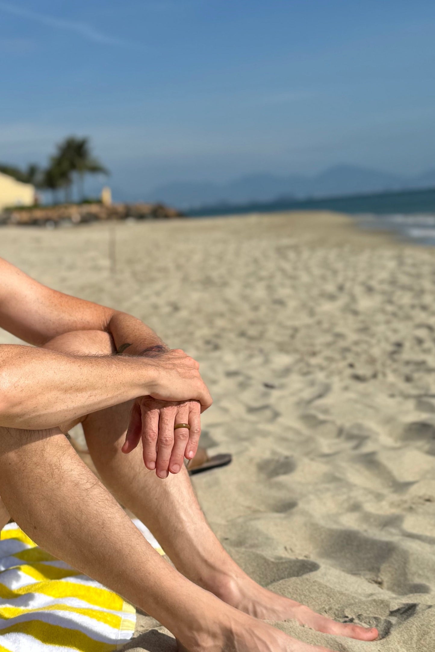 Man sitting on a beach towel under a blue sky