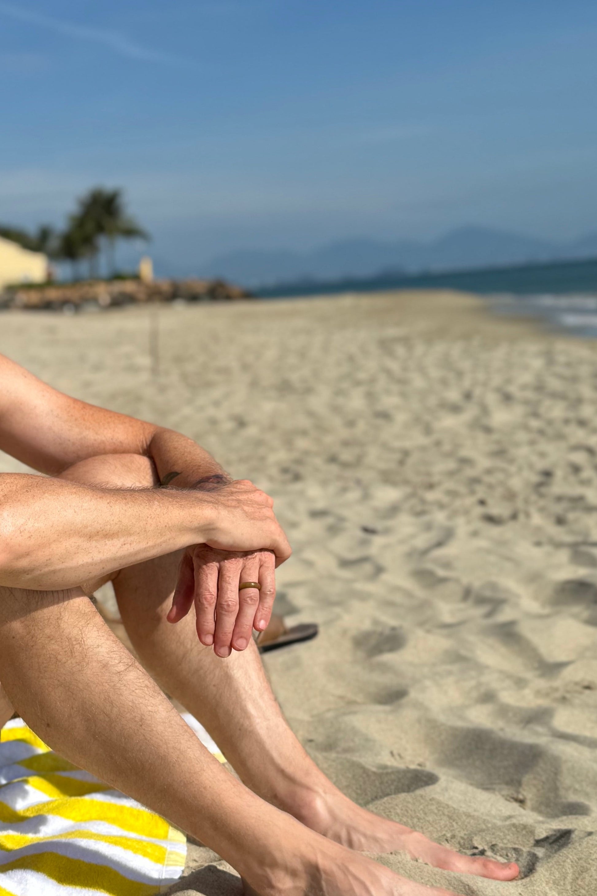 Man sitting on a beach towel under a blue sky