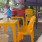 Yellow plastic chairs and tables under a purple canopy with a person in the background.