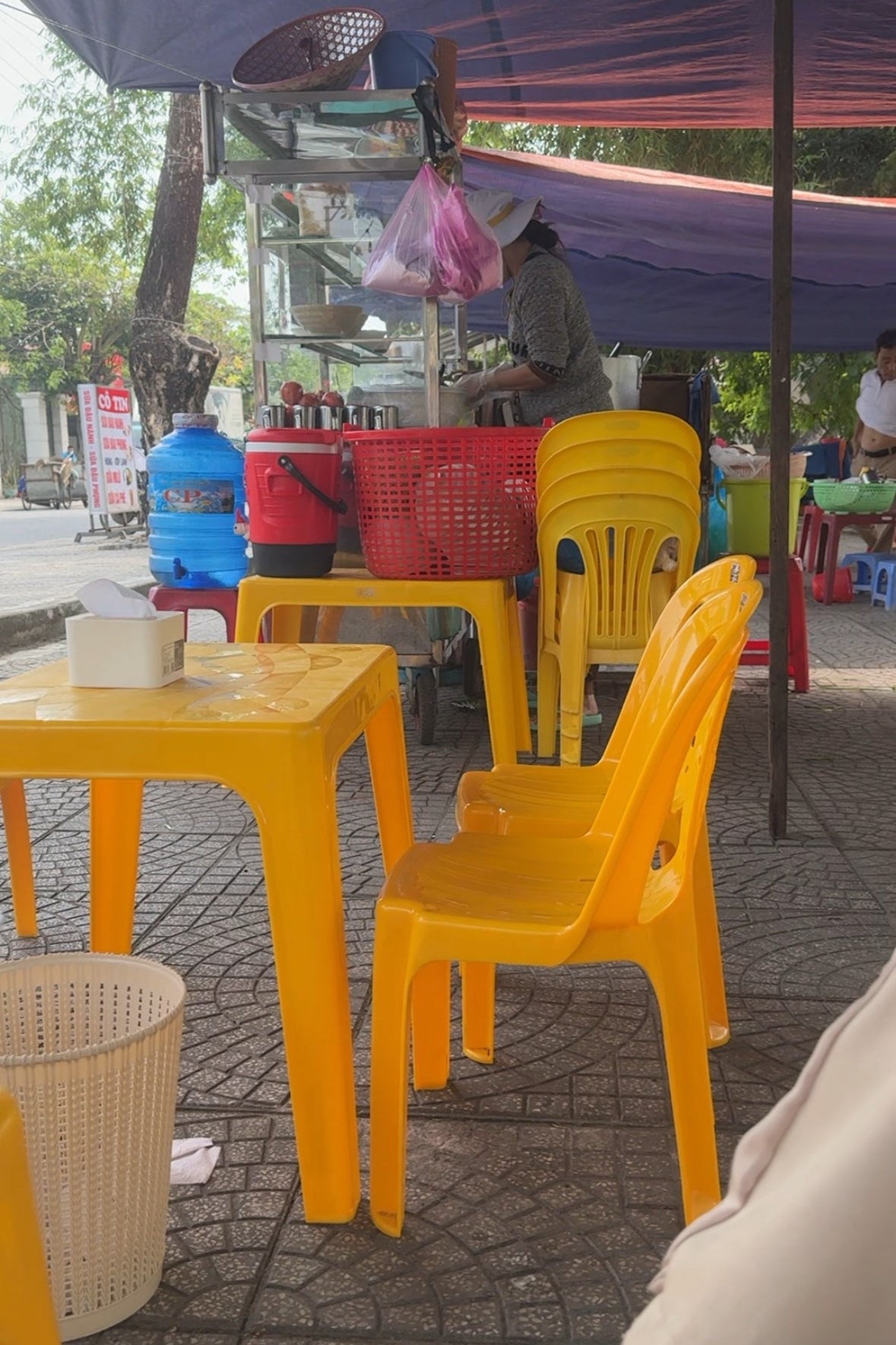 Yellow plastic chairs and tables under a purple canopy with a person in the background.
