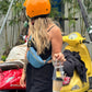 Person wearing an orange helmet and black outfit with a blue bag, standing next to a yellow scooter.