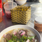 Bowl of pho with vegetables and a person in the background