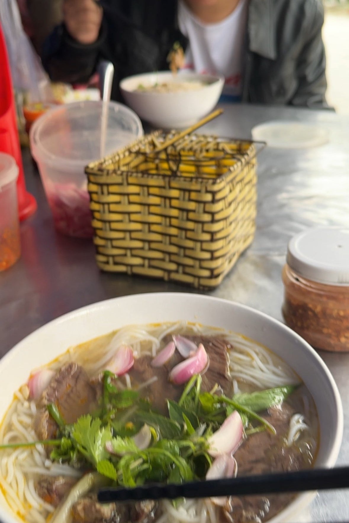Bowl of pho with vegetables and a person in the background